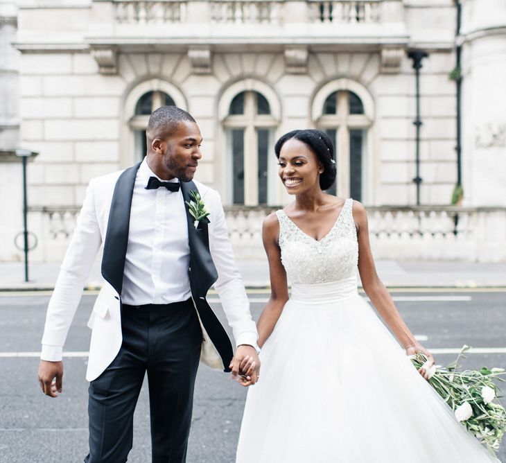 Bride & groom walk together holding hands whilst bride wears Allure Gown