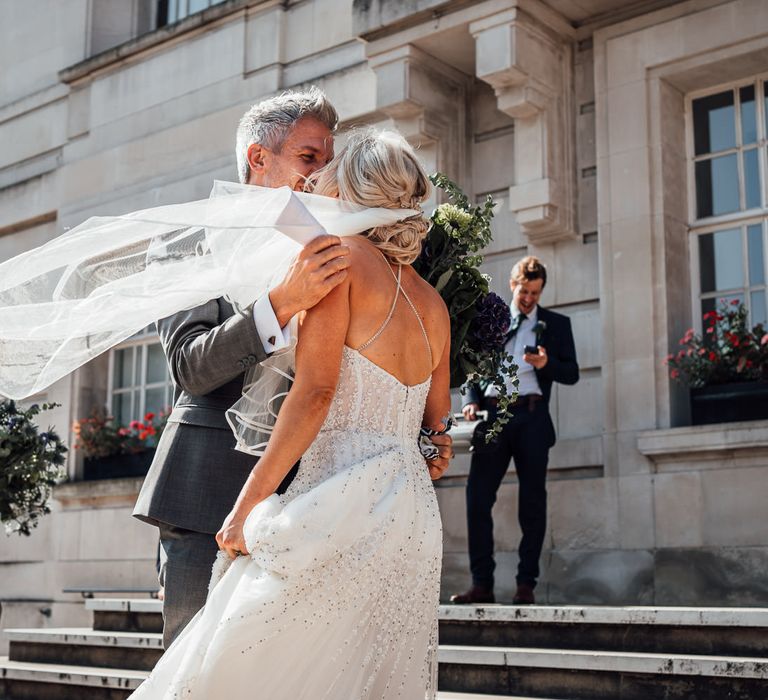 Brides veil blows in the wind as she stands upon the steps of Hackney Town Hall