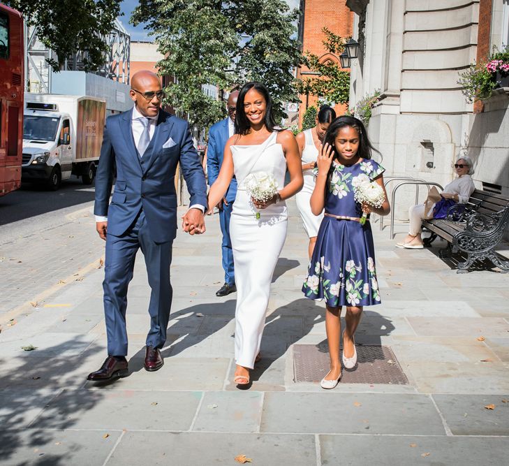 Bride and groom holding hands walking down King's Street in Chelsea with their daughter 