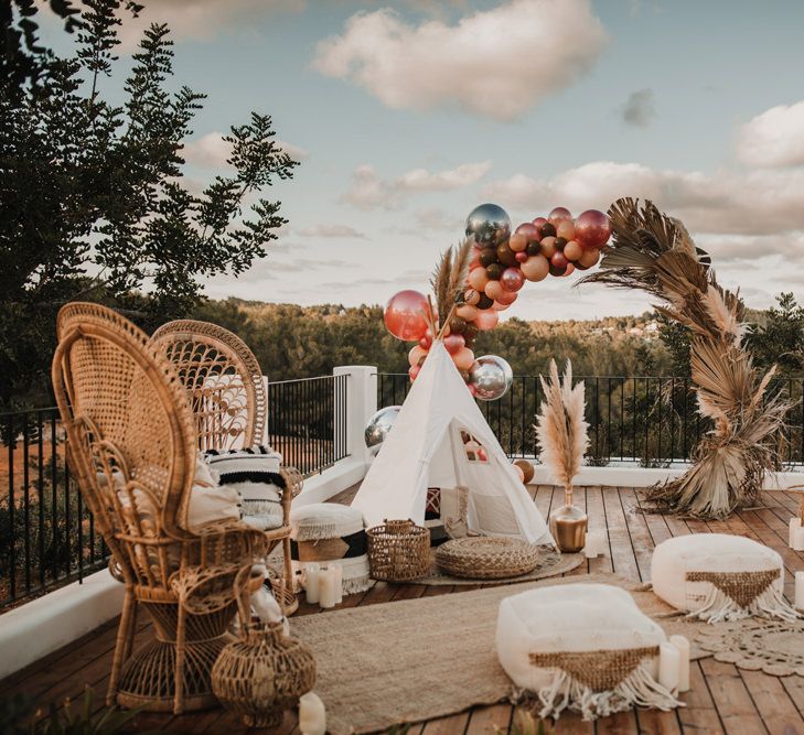 Chill out area with peacock chairs, tipi, cushions and balloon arch 