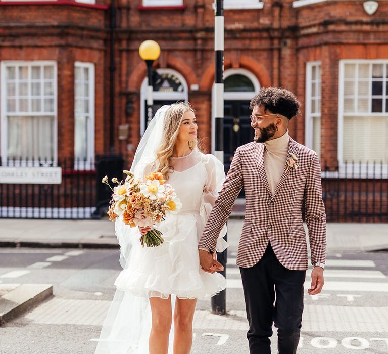 Stylish bride and groom in a short wedding dress and check blazer crossing the street in Chelsea, London 