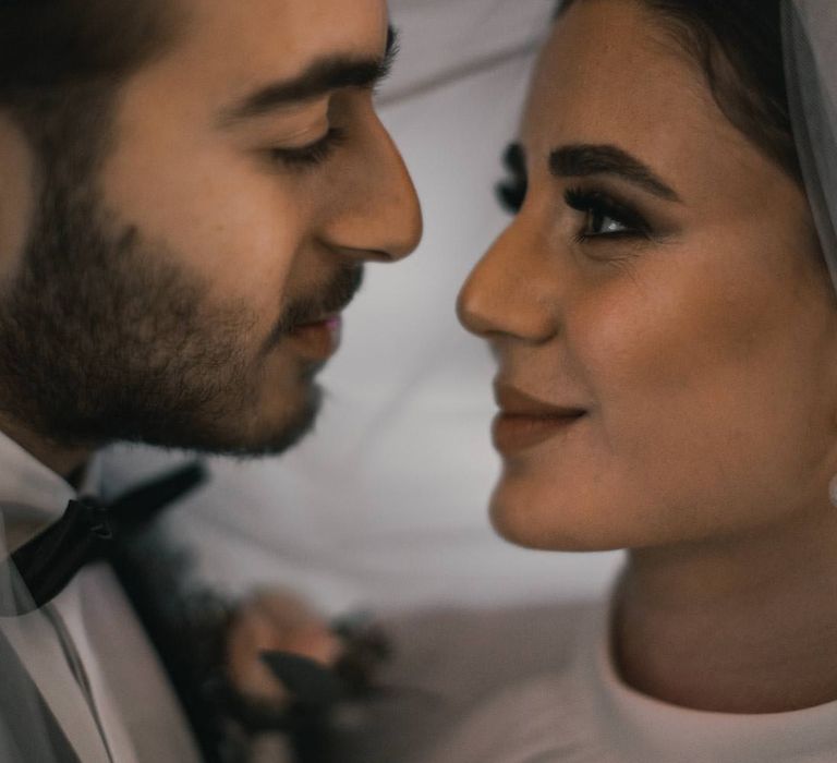 Bride & groom look tenderly at one another whilst standing under brides veil