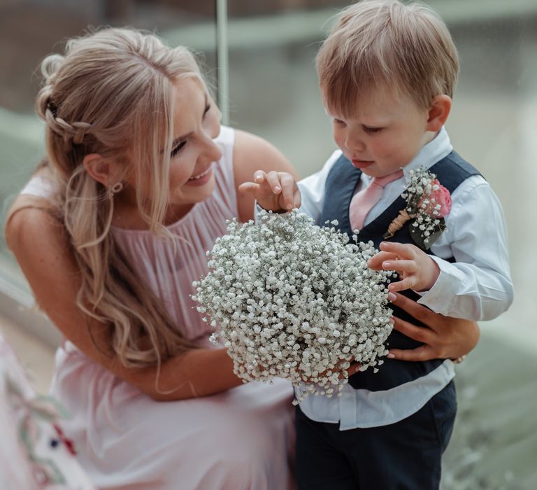 Bridesmaid stands with little boy in suit whilst looking at florals