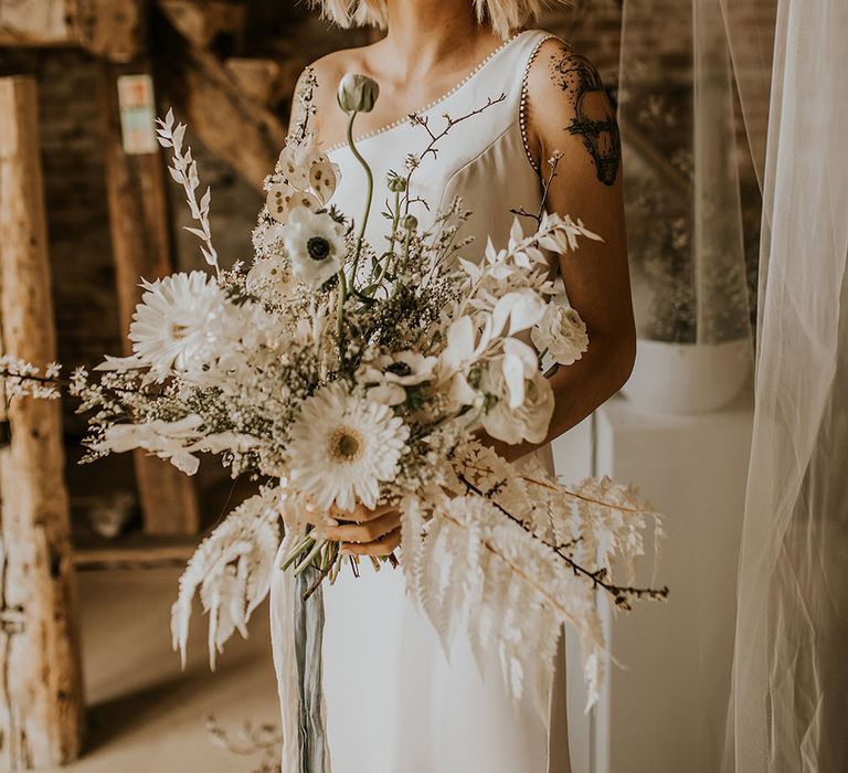 Bride in a one shoulder wedding dress holding a white flower bouquet with gerberas, anemones, poppies and ranunculus 