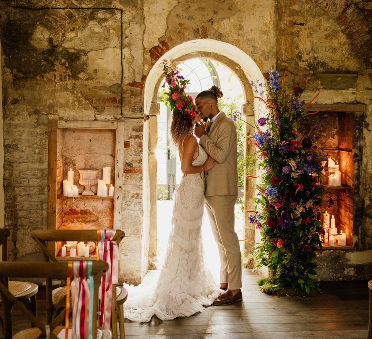 Bride and groom kissing in the intimate ceremony room with pillar candles, vertical floral arrangement and ribbon chair back decor 