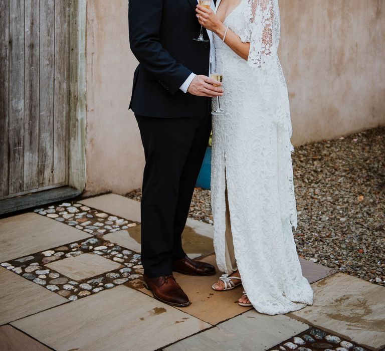 Bride & groom stand with one another on their wedding day whilst bride holds glass of champagne outdoors