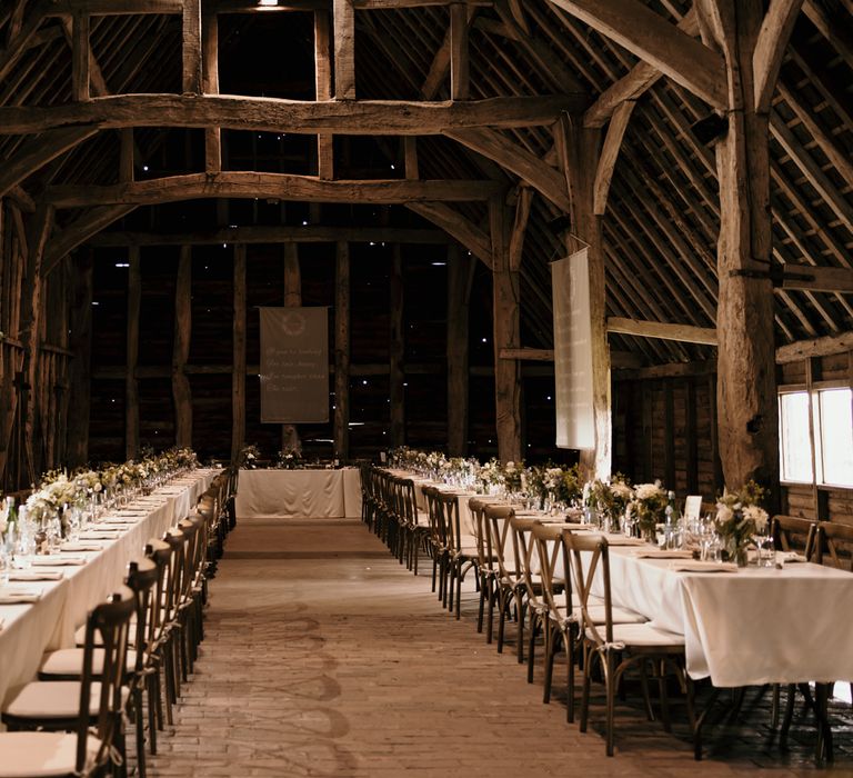 Rustic barn wedding reception with white clothed tables and white floral bouquets