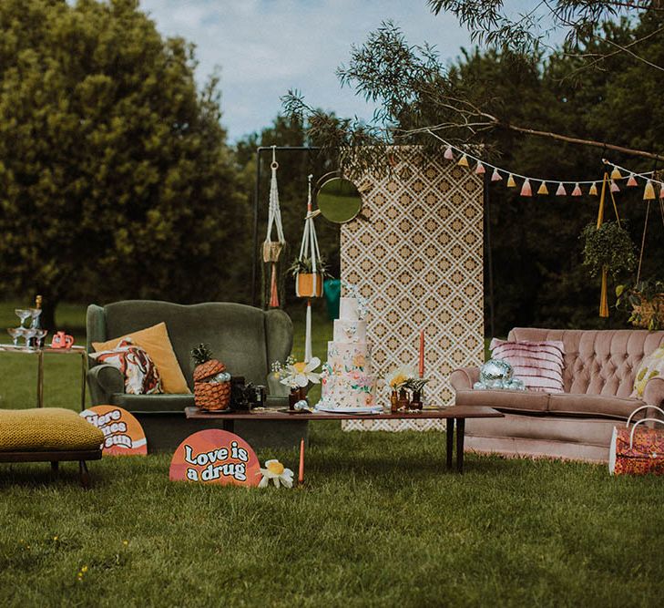 Sixties wedding inspiration outdoor seating area with bold prints, vibrant colours and retro decor including sofas, cushions, macrame, tassels and signs 