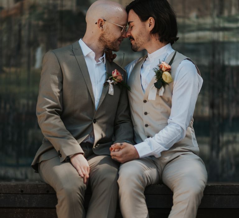 Two grooms embracing on the stage at The Larmer Tree gardens wearing a green suit and beige waistcoat 