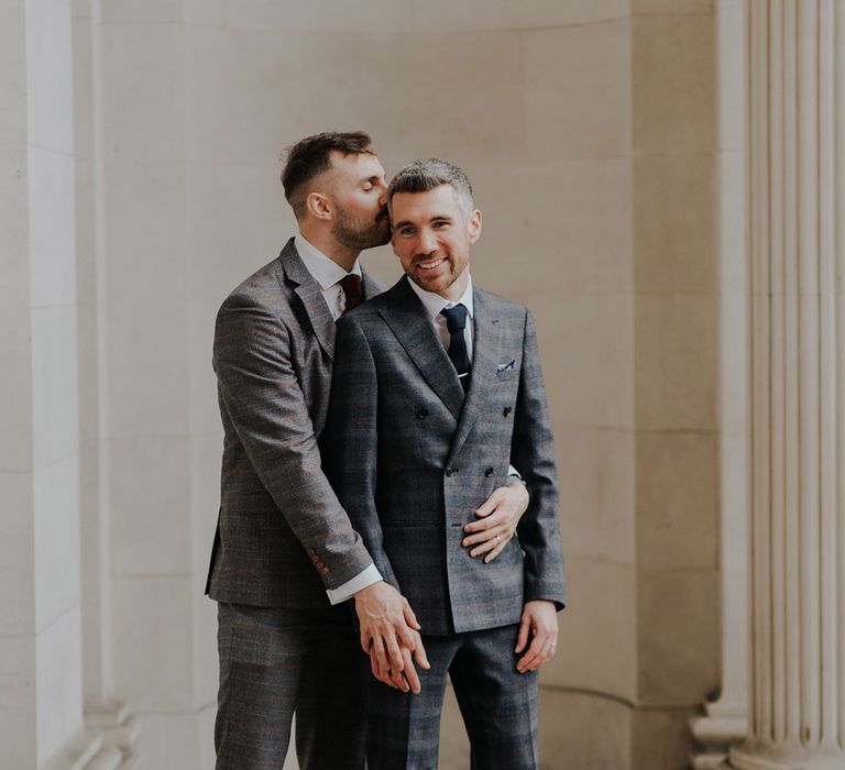 Grooms smile with one another in front of white Pillars for Town Hall wedding day