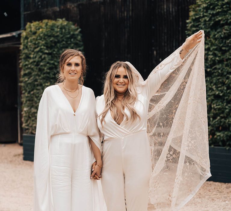 Bride lifts her veil in the air as she walks with her wife on their wedding day