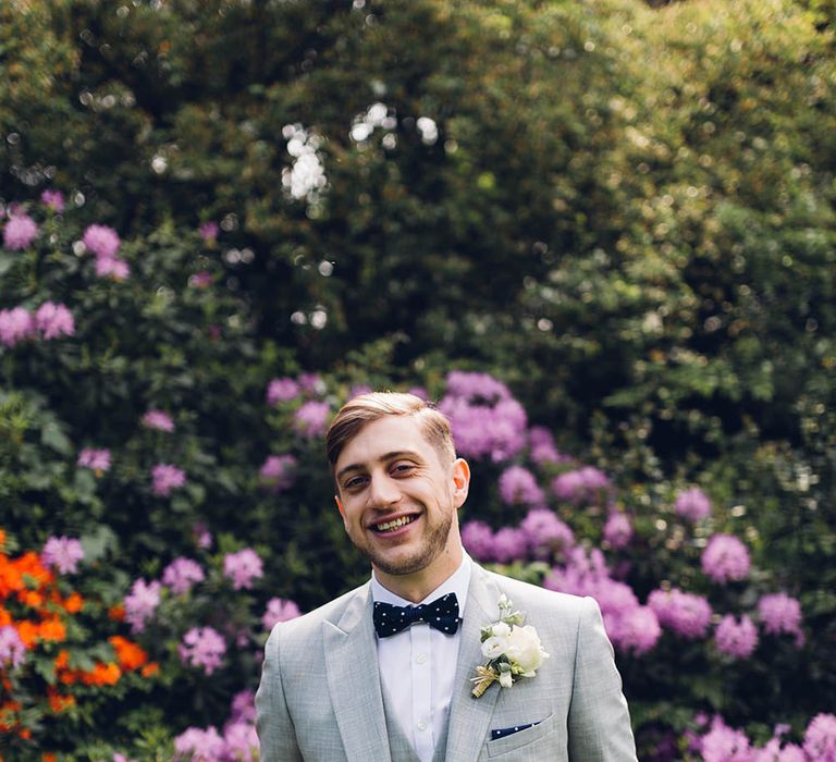 Groom in a pale grey wedding suit and matching waistcoat with navy bow tie and polka dot pocket square