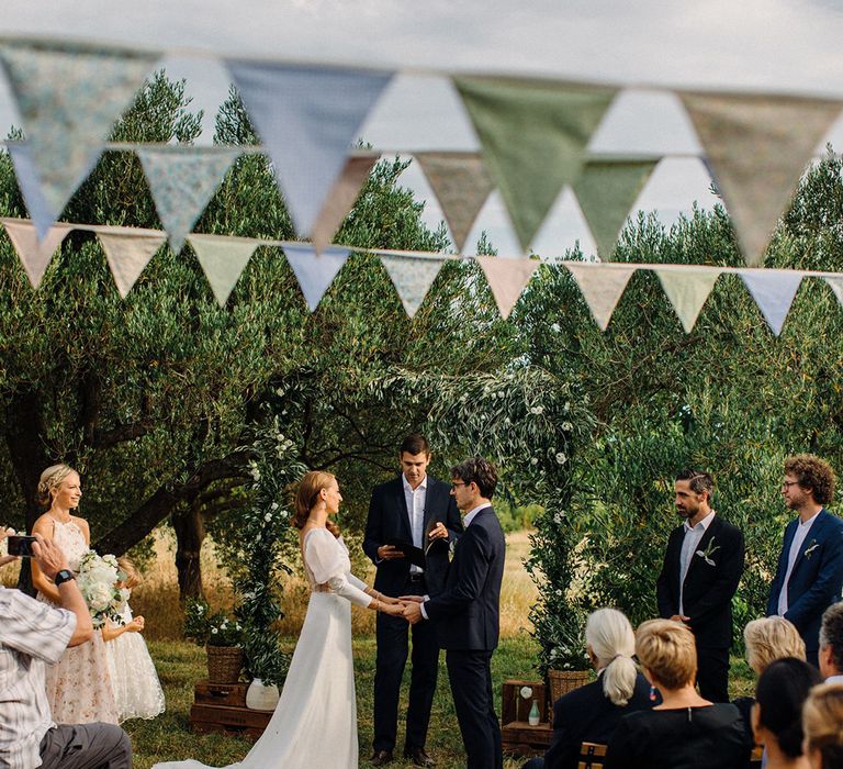 Bride & groom during wedding in Croatia outdoors complete with bunting as wedding guests watch on