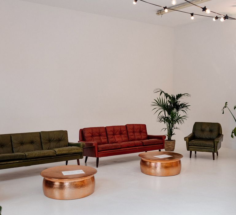 Leather seating with potted plants and round hammered copper coffee tables with festoon lighting inside Loft Studios London for wedding