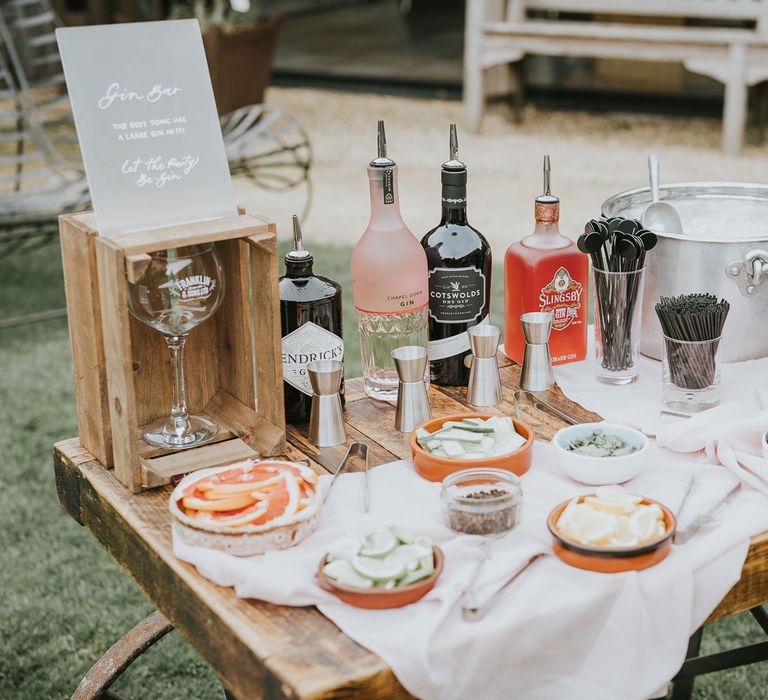 Make your own gin bar with gins, shot measures, garnishes and ice bucket on wooden table for Tythe Barn wedding with barn wedding flowers