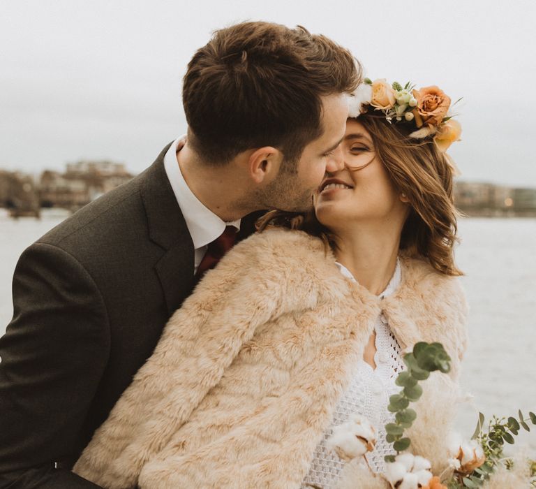 Intimate city wedding at Linden House with bride in a faux fur coat and orange coloured flower crown kissing her groom 