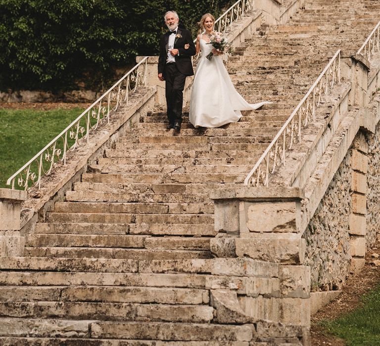 Father of the bride in a black tuxedo and his daughter in a Stella York wedding dress walking down the steps of Chateau Lagorce wedding venue 