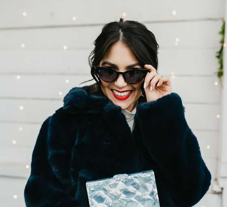 Stylish bride in a navy faux fur coat wearing sunglasses and red lipstick 