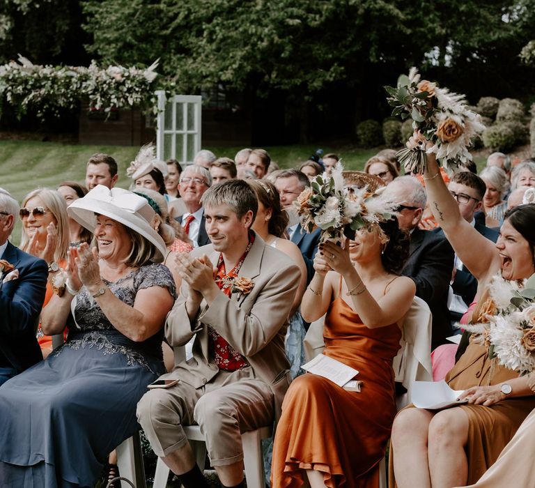 Various wedding guests smile and clap during DIY garden wedding ceremony in Bedfordshire