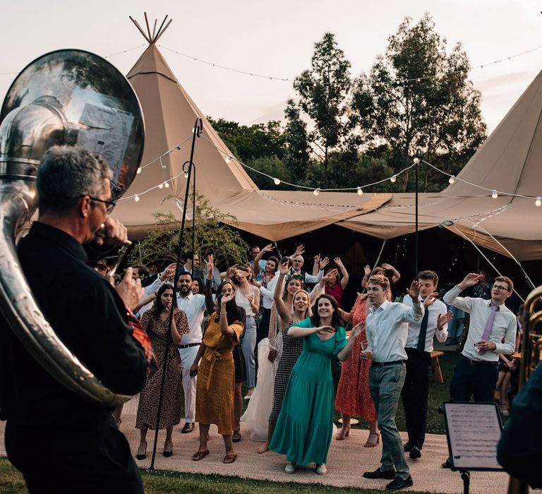 Wedding guests dance outside to brass band during tipi wedding reception 