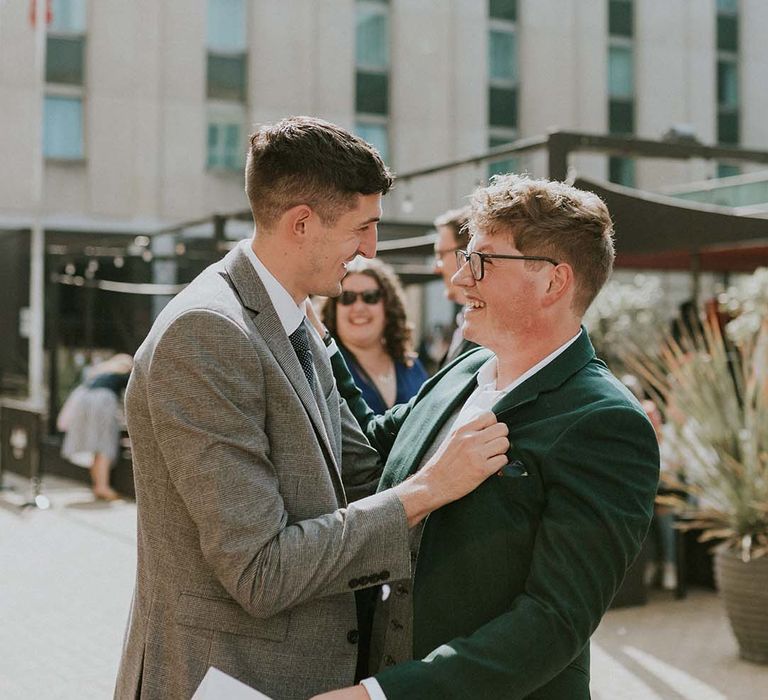 Groom celebrates with wedding guest who holds his jacket and smiles whilst laughing