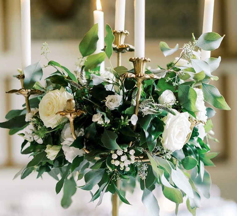 gold candelabra wedding centrepiece decorated with white flower and green foliage 