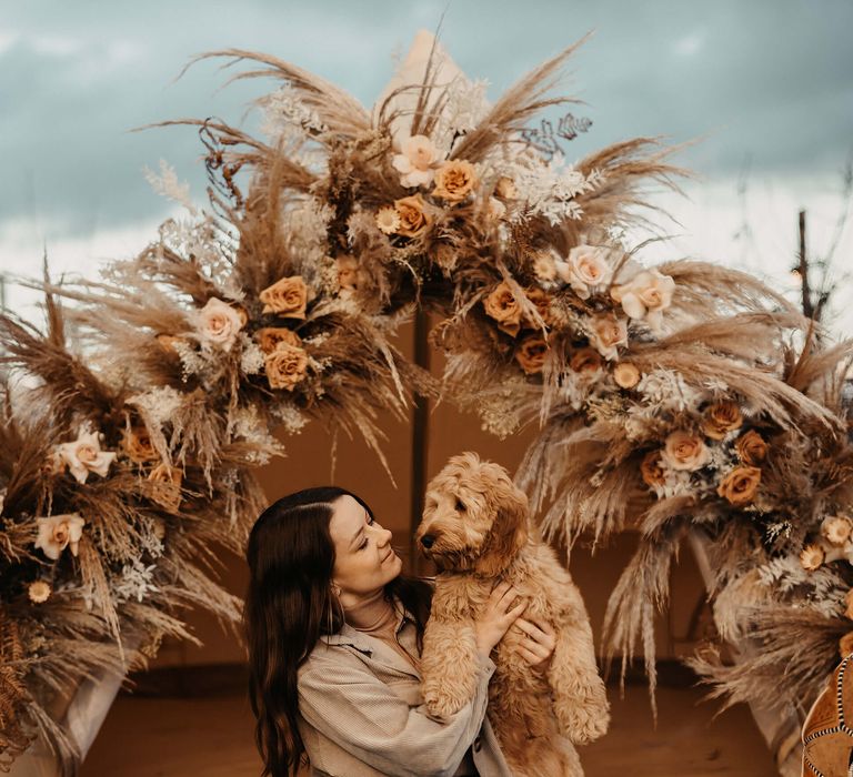 Bride-to-be in blue jeans and a beige cord shirt embracing her cockapoo in a bell tent 