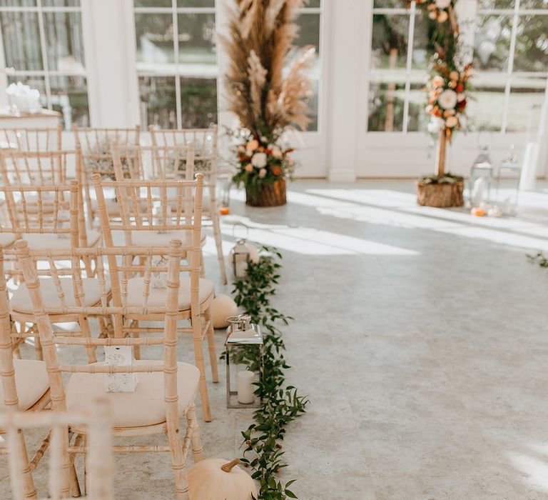 White pumpkins line the aisle with green foliage and lanterns with white candles