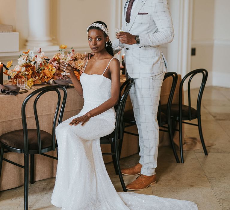 Groom in a stone check suit with brown tie and pocket square standing over his bride at the reception table in a white sparkly wedding dress 