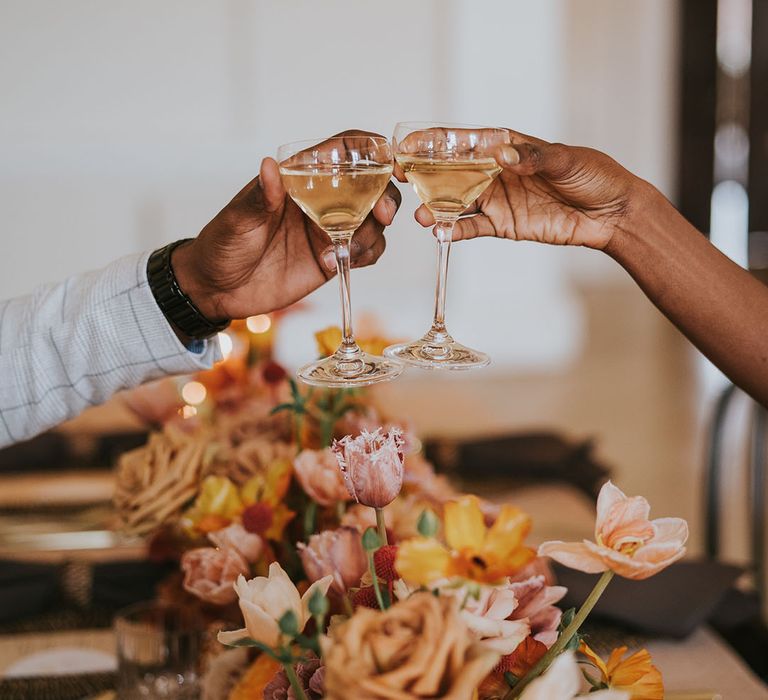 Bride and groom toasting champagne over an orange flower centrepiece 