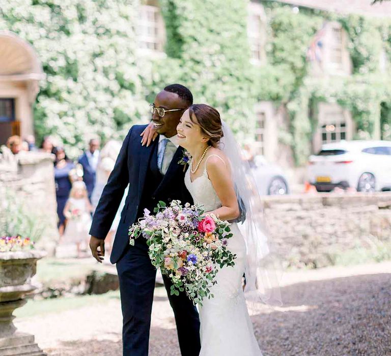 Bride & groom wrap their arms around one another as bride holds pastel floral bouquet 