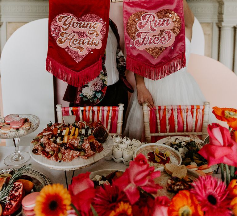 Two brides holding up velvet banners with tassels saying Young Hearts, Run Free