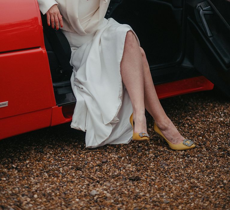 Bride sits in vintage Ferrari on her wedding day and wears yellow Malono Blahnik heels 