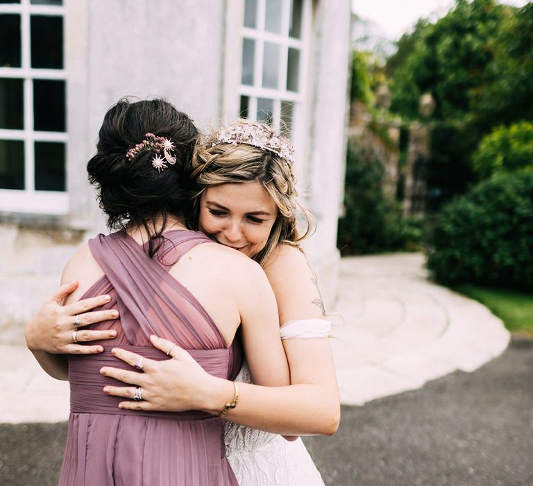 Bride hugs a bridesmaid in taupe pleated bridesmaid dress