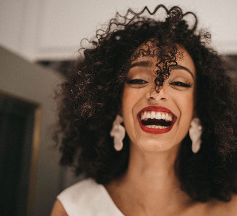 Black bride with naturally curly hair wearing dangly earrings and wearing red lipstick 