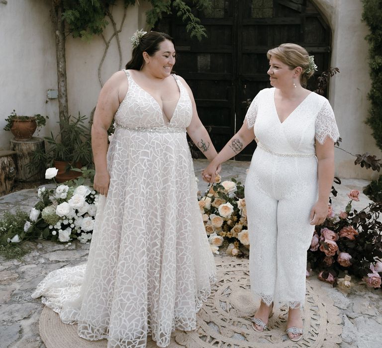 Brides hold hands wearing white on cream circular rugs at altar in Barcelona