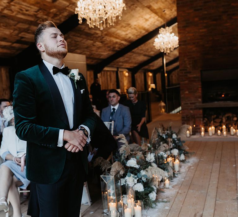 Groom in black tie including green velvet suit jacket nervously awaits the arrival of the bride at winter Christmas wedding