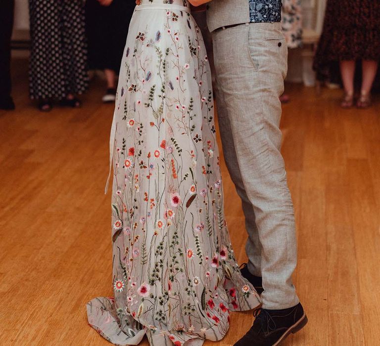 Bride in floral embroidered wedding dress dances with groom in grey and blue patterned waistcoat 