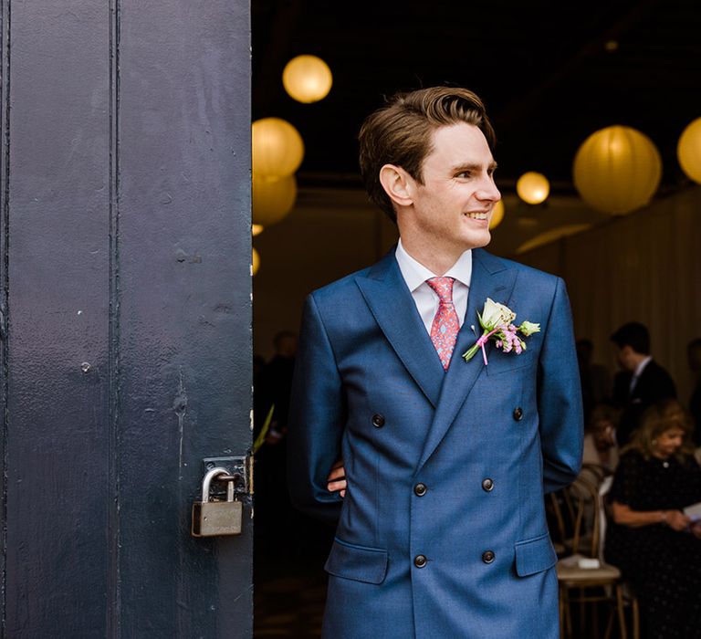 Groom in double breasted blue suit with pink and blue patterned tie and white rose buttonhole for city wedding