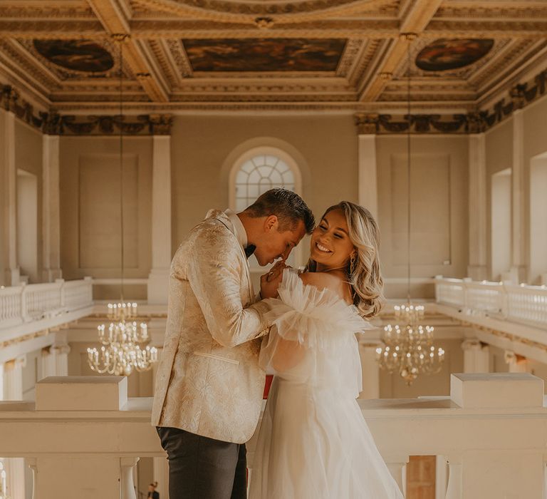 Groom kisses the brides hands as she smiles brightly in Halfpenny London wedding dress at the Banqueting House in London