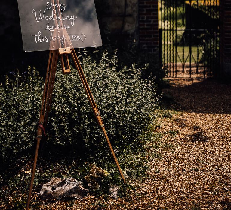 Clear wedding sign directing guests to the evening reception on easel 