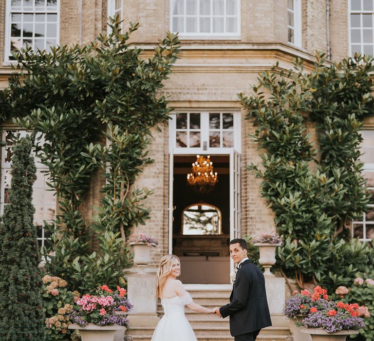 Bride and groom hold hands and look back at the camera 