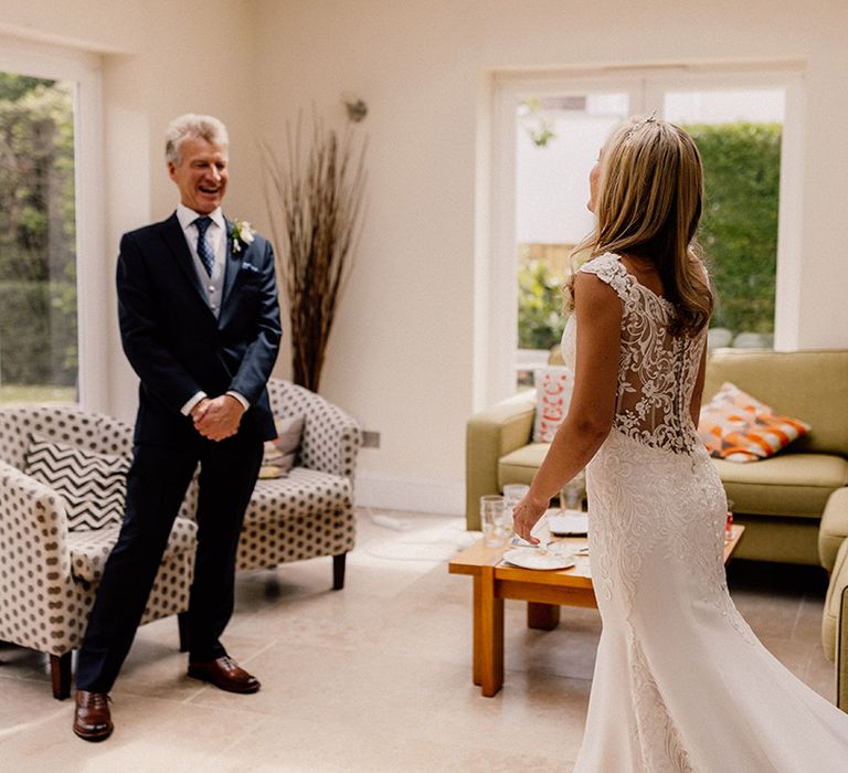 Bride enters the room wearing her sheer lace back wedding dress with button detail as father of the bride gets his first look 