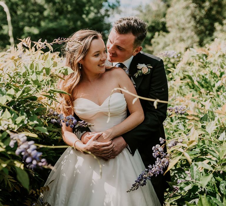 Groom wraps his arms around his bride who wears Suzanne Neville wedding dress with sweetheart neckline