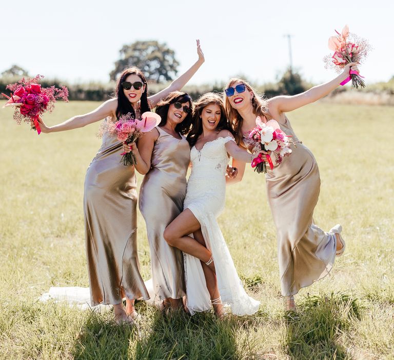 Bridesmaids wear sunglasses and hold out bright floral bouquets whilst wearing champagne bridesmaid dresses outdoors 