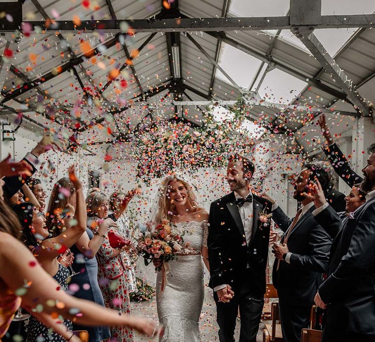 Bride in lace boho two piece and groom in black tux with bow tie and boutonniere doing confetti walk at Hackney Studios