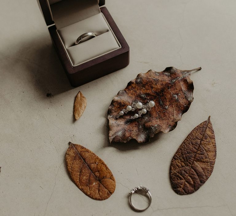 Pearl earrings on leaf beside silver wedding band