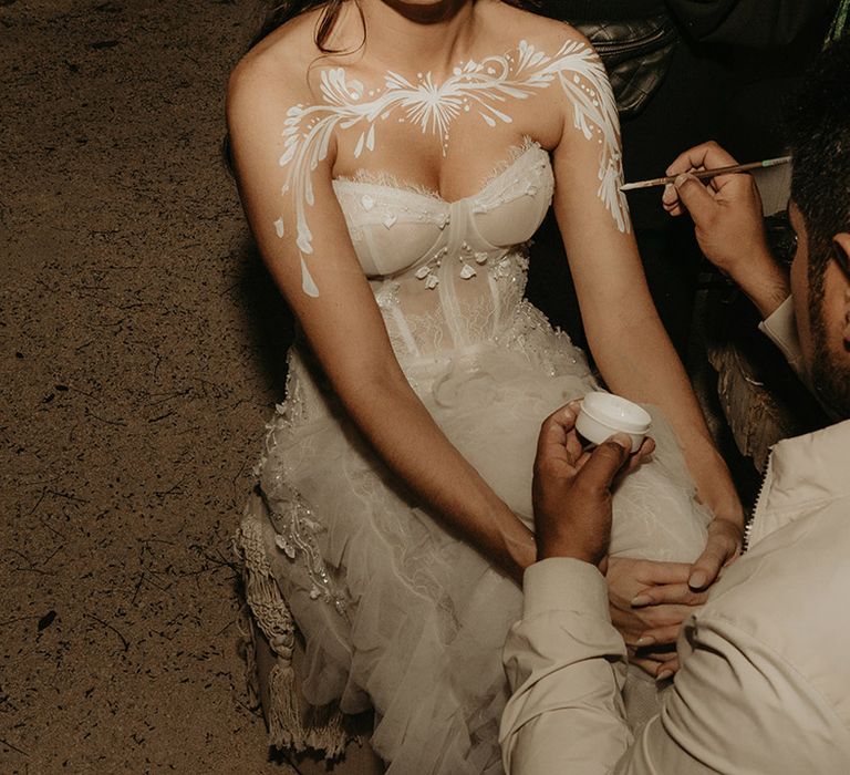 Bride has her décolletage painted white for reception rave in the jungle  