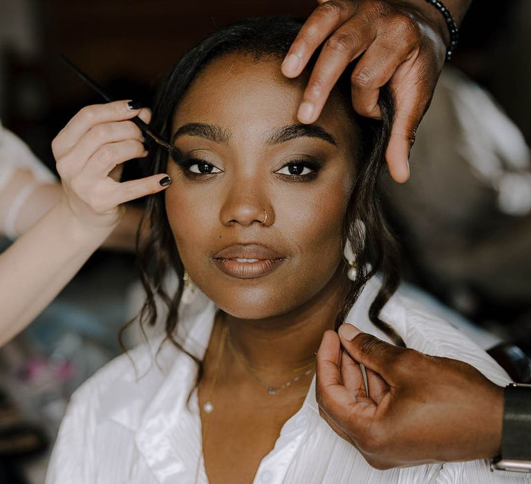 Black Bride in white satin shirt and a gold pearl necklace having her hair and make up done