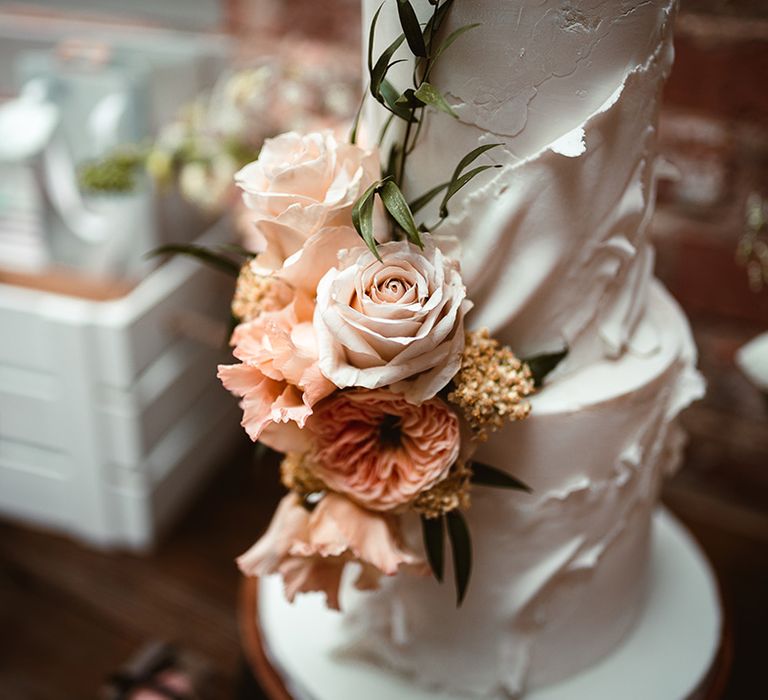 Two tiered buttercream wedding cake with icing details and light pink rose, peony, foliage and golden decorations 